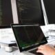 A developer working on a laptop between two monitors showing code