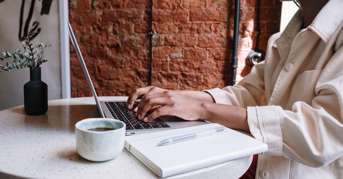 A person typing on a laptop at a cafe table with coffee