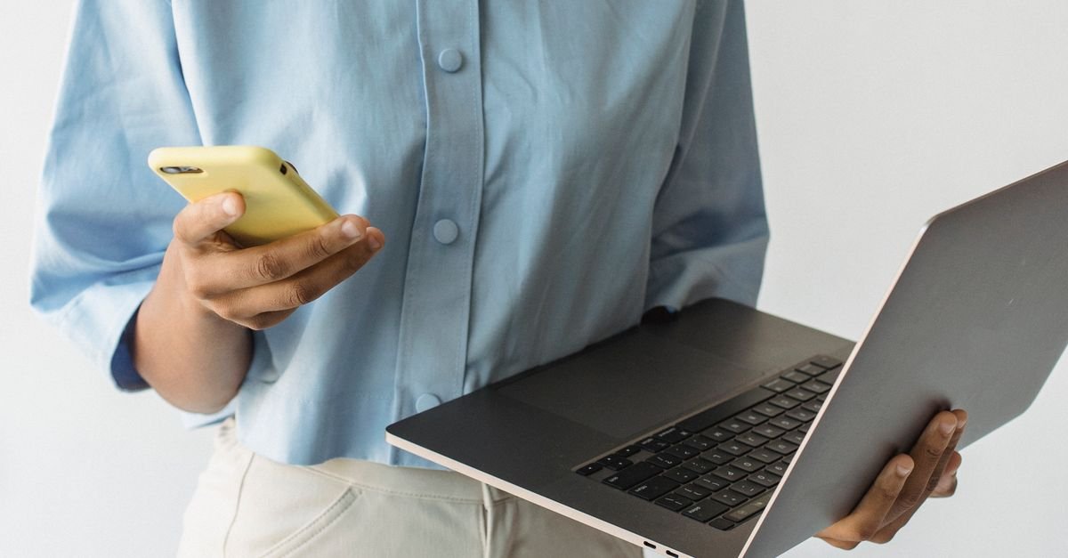 A person holding a phone and a laptop