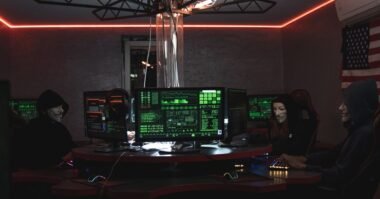 A dark security operations room with monitors showing green code