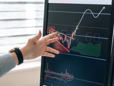 A hand pointing at a rising chart on a screen