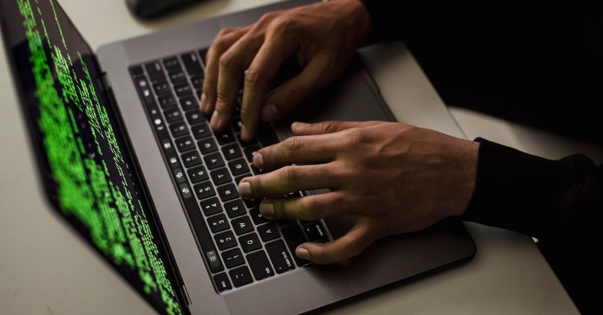 Hands typing on a laptop showing green code