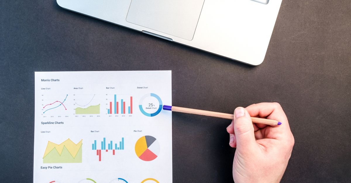 A hand pointing at printed charts beside a laptop
