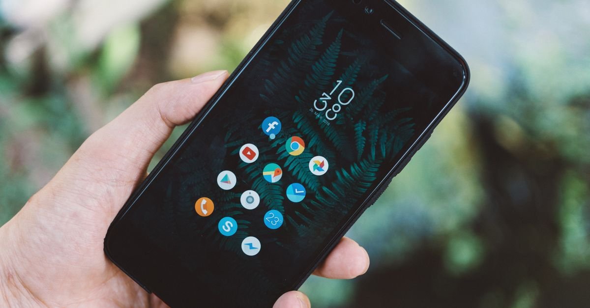 A hand holding a smartphone with a grid of apps
